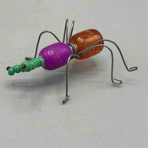 May include: A wire sculpture of a bug with a purple, green, and orange body. The bug has six legs and is made of wire and beads.