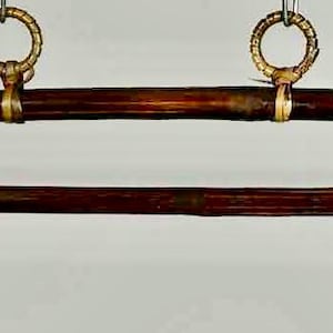 May include: A dark brown, curved wooden object with a straight, parallel wooden piece below it. Both pieces are connected by gold-colored metal bands and suspended from two gold-colored rings. The wood has a natural grain and a polished finish.