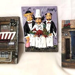 May include: Three decorative wall plaques featuring detailed, colorful scenes. One depicts a shop with a red and white awning, another shows three chefs, and the third displays a bookstore with the word "LIVRES".