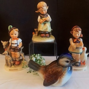 May include: A set of four porcelain figurines, including a girl with a book, a boy with two goats, a girl with a bird, and a bluebird. The figurines are all hand-painted and feature intricate details.