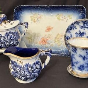 May include: A porcelain tea set featuring a sugar bowl with a lid, a creamer, a teacup with a saucer, and a rectangular tray. The pieces are decorated with blue and white floral patterns, gold trim, and hand-painted orange flower accents.