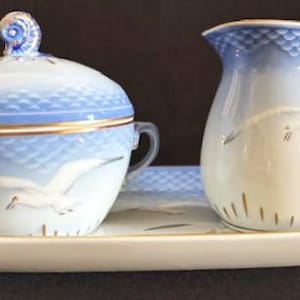 May include: A porcelain tea set with a sugar bowl, creamer, and serving tray. The set features a blue and white color scheme with a seagull design. The sugar bowl has a lid with a decorative handle. The creamer has a handle and spout.