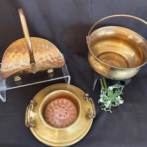 以下が含まれることがあります： アンティークの真鍮製のボウルが3つ。1つのボウルはハンドルが付いており、バスケットの形をしています。もう1つのボウルは丸い縁と銅の内側を持っています。3つ目のボウルは丸く、ハンドルが付いています。