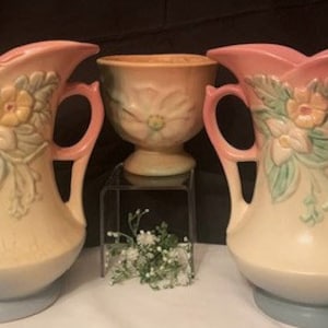 Puede incluir: Dos jarrones de cerámica vintage con diseños florales en tonos rosa, amarillo y verde. Los jarrones tienen dos asas y una base de color crema.