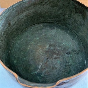 May include: A copper bowl with a green patina inside. The bowl has a slightly uneven rim and a worn surface.