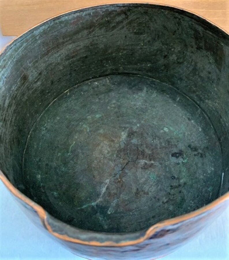 May include: A copper bowl with a green patina inside. The bowl has a slightly uneven rim and a worn surface.