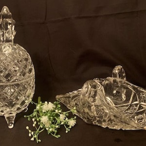 Könnte beinhalten: Zwei durchsichtige gläserne Ananasförmige Schalen mit aufwendigen geschliffenen Glasmustern. Die größere Schale hat einen Deckel und steht auf drei Beinen. Die kleinere Schale ist offen und hat einen Griff.