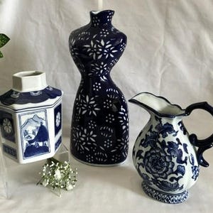 Pode incluir: Uma coleção de três peças de cerâmica com padrões em azul e branco. Inclui um pote hexagonal com ilustrações de paisagens, um vaso em forma de torso com motivos florais e um jarro com desenhos florais detalhados.