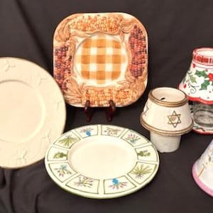 Puede incluir: Una colección de platos decorativos y candelabros. Incluye un plato redondo grande de color crema con diseños florales en relieve, un plato cuadrado con un centro de cuadros y varios candelabros pequeños con varios diseños.