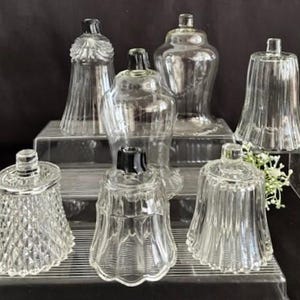 Puede incluir: Una colección de candelabros de vidrio transparente con tapas negras. Los candelabros tienen varias formas, incluyendo diseños en forma de campana, con patrones de diamantes y acanalados. Están dispuestos sobre soportes de exhibición transparentes y escalonados.