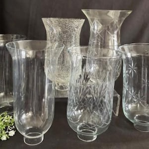 May include: Set of six clear glass candle holders with various patterns. The holders are all different shapes and sizes, and some have a textured or ribbed surface.