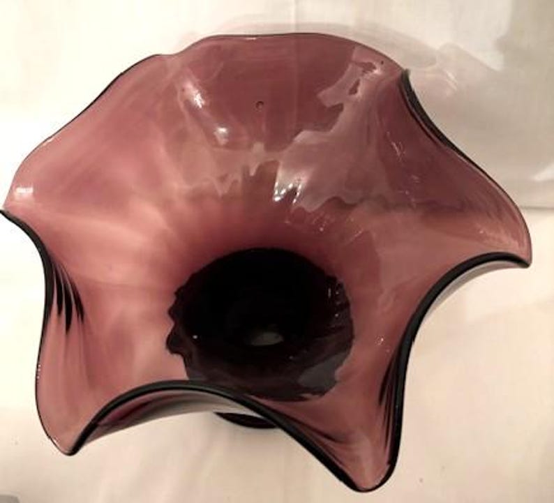 Puede incluir: Un jarr&oacute;n de vidrio morado grande con una abertura ancha y acampanada y un borde rizado. El jarr&oacute;n est&aacute; hecho de vidrio transparente con un tinte morado oscuro.