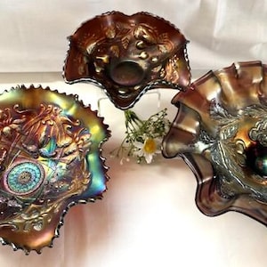 Puede incluir: Tres cuencos de vidrio de carnaval iridiscente con bordes ondulados y patrones florales y de hojas en relieve. El vidrio presenta un acabado metálico oscuro con tonos cambiantes de púrpura, bronce y verde que reflejan la luz en las superficies.