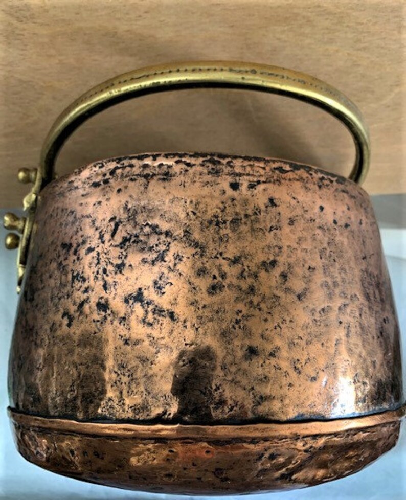 May include: A vintage copper pot with a brass handle. The pot has a hammered finish and a worn patina.