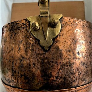 May include: A vintage copper pot with a brass handle. The pot has a hammered finish and is showing signs of age.