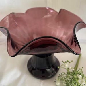 Puede incluir: Un cuenco de vidrio morado con un borde rizado y una base de pedestal. El cuenco est&aacute; hecho de vidrio transparente con un tinte morado.