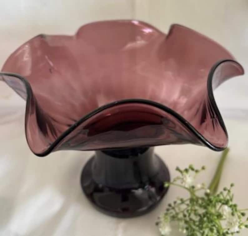 Puede incluir: Un cuenco de vidrio morado con un borde rizado y una base de pedestal. El cuenco est&aacute; hecho de vidrio transparente con un tinte morado.