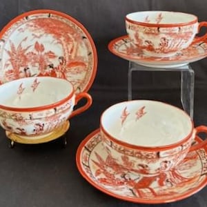 Peut inclure: Un ensemble de quatre tasses à thé et soucoupes vintage. Les tasses et les soucoupes sont blanches avec un motif paysager rouge d'inspiration asiatique. Chaque tasse a une anse et repose sur une soucoupe assortie.