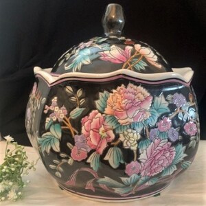 May include: A black porcelain lidded jar with a scalloped rim and floral design. The jar is decorated with pink, blue, and green flowers on a black background.