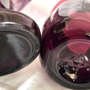 Puede incluir: Dos jarrones de vidrio morado con una superficie texturizada. Los jarrones son redondos y tienen una base ancha.
