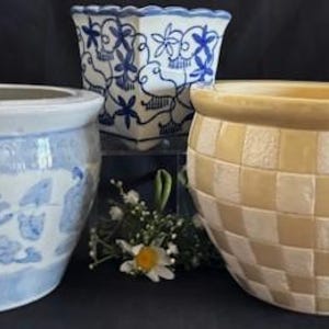Puede incluir: Tres macetas de cerámica. Una es redonda con un diseño floral azul y blanco. Otra tiene forma cuadrada con un patrón de pájaros y flores azules y blancos. La tercera es una maceta redonda con un patrón a cuadros en crema y blanco.