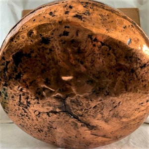 May include: The bottom of a large copper pot with a hammered finish. The copper has a warm, reddish-brown color and shows signs of age and use.