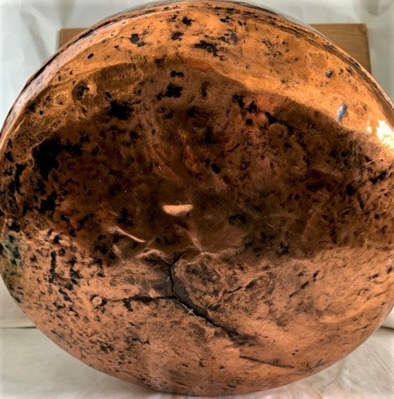 May include: The bottom of a large copper pot with a hammered finish. The copper has a warm, reddish-brown color and shows signs of age and use.