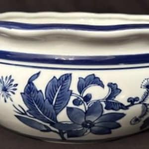 Könnte beinhalten: Eine weiße Keramikschale mit gewelltem Rand und einem tiefblauen, gemalten Blumenmuster. Das Design zeigt detaillierte Blätter, Blüten und sternförmige Akzente, die die Außenseite umgeben, ergänzt durch ein durchgehendes blaues Band am oberen Rand.