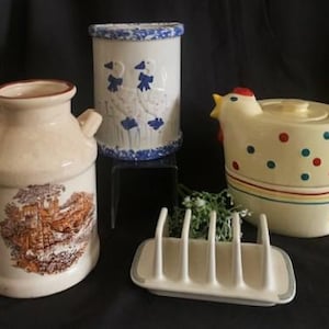 Może przedstawiać: Zestaw czterech zabytkowych ceramicznych artykułów kuchennych, w tym dzbanek na mleko, pojemnik z niebieskim i białym wzorem kwiatowym, czajnik w kształcie kurczaka z czerwonymi i niebieskimi kropkami oraz biały ceramiczny toster.