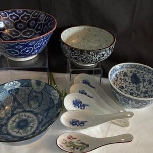 Puede incluir: Un juego de cinco cuencos de cerámica azul y blanca con diseños florales y geométricos, y cinco cucharas de cerámica blanca con diseños florales azules y verdes.