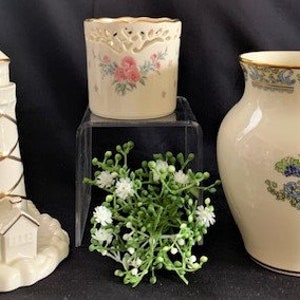 Può includere: Tre pezzi decorativi in ceramica: un faro bianco con accenti dorati, un vaso bianco con un motivo floreale e un portacandele bianco con un motivo floreale.