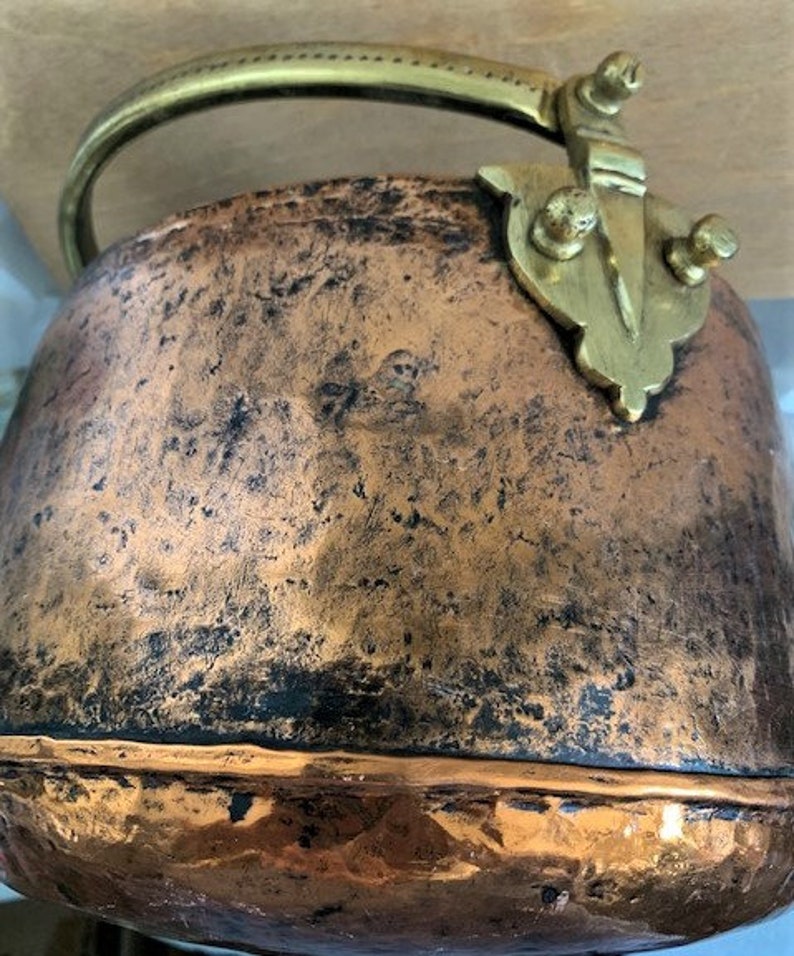 May include: A vintage copper pot with a brass handle and decorative brass accents. The pot has a worn, aged patina and a hammered texture.