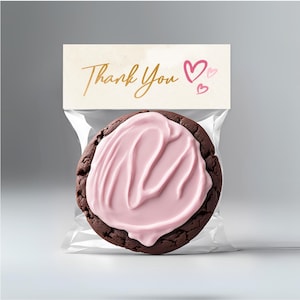 May include: A chocolate cookie with pink frosting in a clear plastic bag with a thank you tag. The tag has gold lettering and pink hearts.