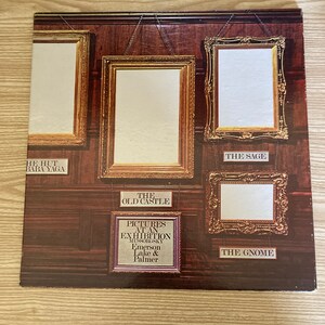 May include: A vintage vinyl record album cover featuring a wood-paneled wall with five ornate gold picture frames. The album is titled "Pictures at an Exhibition" by Mussorgsky, performed by Emerson, Lake & Palmer.
