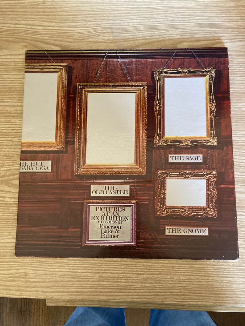May include: A vintage vinyl record album cover featuring a wood-paneled wall with five ornate gold picture frames. The album is titled "Pictures at an Exhibition" by Mussorgsky, performed by Emerson, Lake & Palmer.