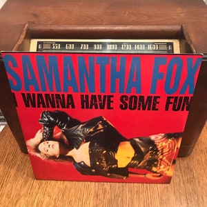 Può includere: Copertina dell'album in vinile di Samantha Fox, intitolato "I Wanna Have Some Fun". La copertina è rossa con testo blu e presenta una foto di una donna in un completo di pelle nera. L'album è appoggiato su una radio vintage in legno.