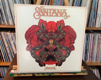 May include: A vintage vinyl record album cover featuring the band Santana. The cover art is a psychedelic design with a red rose and two green snakes. The album title "Festival" is printed in gold lettering at the bottom of the cover.