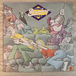 Könnte beinhalten: Eine Cartoon-Illustration einer Band, die Musik spielt. Die Bandmitglieder sind alle in verschiedenen Kostümen gekleidet und sitzen auf einer Couch. Der Text "You should see the rest of the band" befindet sich oben im Bild. Der Text "David Bromberg Band" befindet sich in der Mitte des Bildes. Der Text "Calvin Wilson" befindet sich unten im Bild.