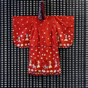 May include: A red kimono with white polka dots and a pattern of girls holding balloons. The kimono has a traditional Japanese design.
