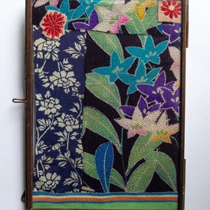 May include: A framed collage of colourful fabric scraps with floral patterns. The fabric is arranged in a patchwork style, with different colours and textures. The frame is made of brass and has a simple design.