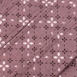 May include: A mauve fabric featuring a repeating geometric pattern of small dark brown four-pointed stars and larger white four-pointed diamond shapes arranged in a grid. The textile has a visible woven texture with diagonal stitched seams.