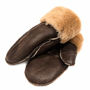 Könnte beinhalten: Ein Paar braune Lederfäustlinge mit einem hellbraunen Pelzbündchen. Die Fäustlinge sind aus dunkelbraunem Leder gefertigt und haben eine genähte Naht an den Rändern. Das Pelzbündchen ist hellbraun.