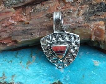 May include: A silver pendant with a geometric design and inlaid red, orange, and brown stones. The pendant is shaped like a triangle and has a loop at the top for attaching a chain.
