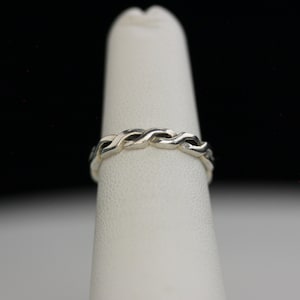 May include: A silver braided ring on a white display stand.