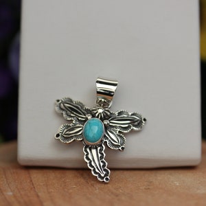 May include: A silver dragonfly pendant with a turquoise stone in the center. The dragonfly has intricate details and a bail for attaching to a chain.