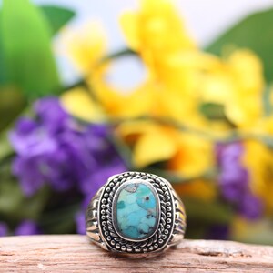 May include: A silver ring with a turquoise stone set in a detailed oval bezel. The ring is surrounded by a decorative rope-like design.
