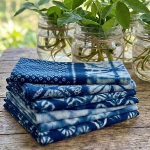 A stack of hand-dyed shibori fabric in various shades of blue and aqua, demonstrating the multi-color possibilities of a home natural dye garden kit and craft project.