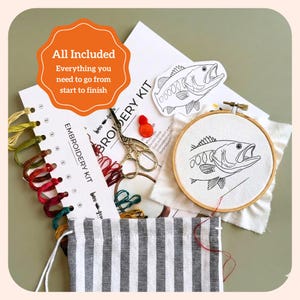 Puede incluir: Un kit de bordado que incluye un bastidor de madera con un dise&ntilde;o de pez sobre tela blanca, un organizador de hilos numerado con hilos de colores, tijeras doradas, una pegatina de pez y una bolsa de rayas grises y blancas.