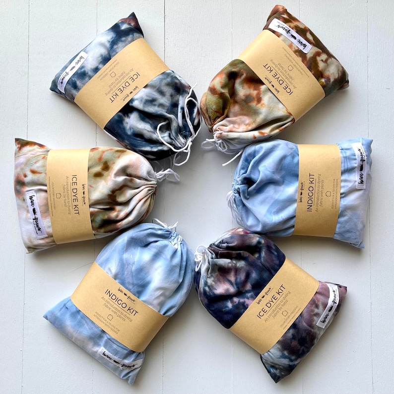 Pode incluir: Uma cole&ccedil;&atilde;o de seis kits de tingimento de tecido, cada um em um saco com cord&atilde;o e embrulhado com uma etiqueta de papel marrom. Os kits apresentam padr&otilde;es tie-dye em tons de azul, marrom e cinza. Os r&oacute;tulos dizem "ICE DYE KIT" e "INDIGO KIT".