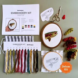 May include: An embroidery kit featuring a rainbow trout pattern, including a wooden hoop with a finished trout design, a second hoop with a printed trout outline, embroidery floss in various colors, scissors, needles, and instructional paper.